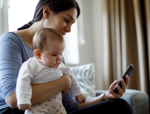 Mother holding daughter while taking care of business on her phone