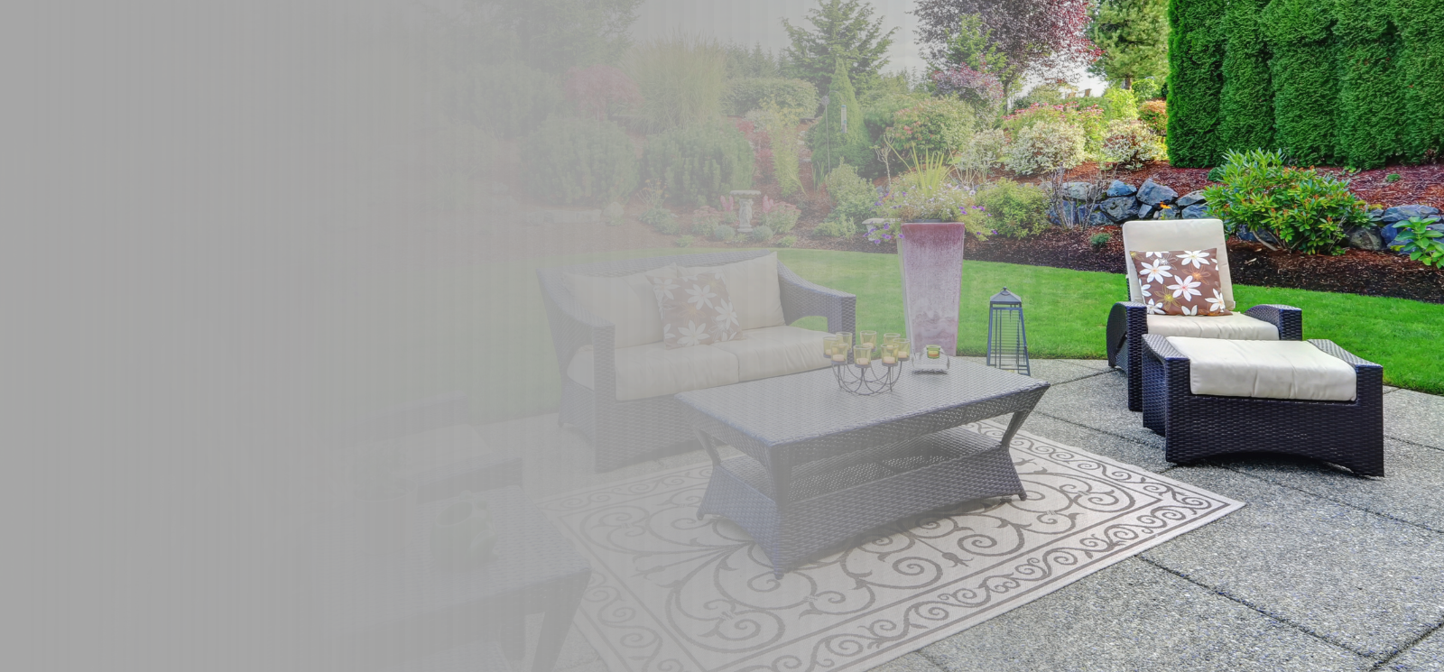 Blank background image with grey fade on left and patio set against lush green landscaping on right.
