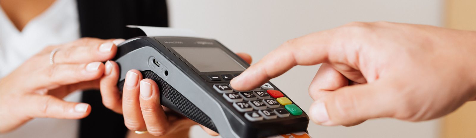 hands holding a credit card terminal while additional hands type in a PIN